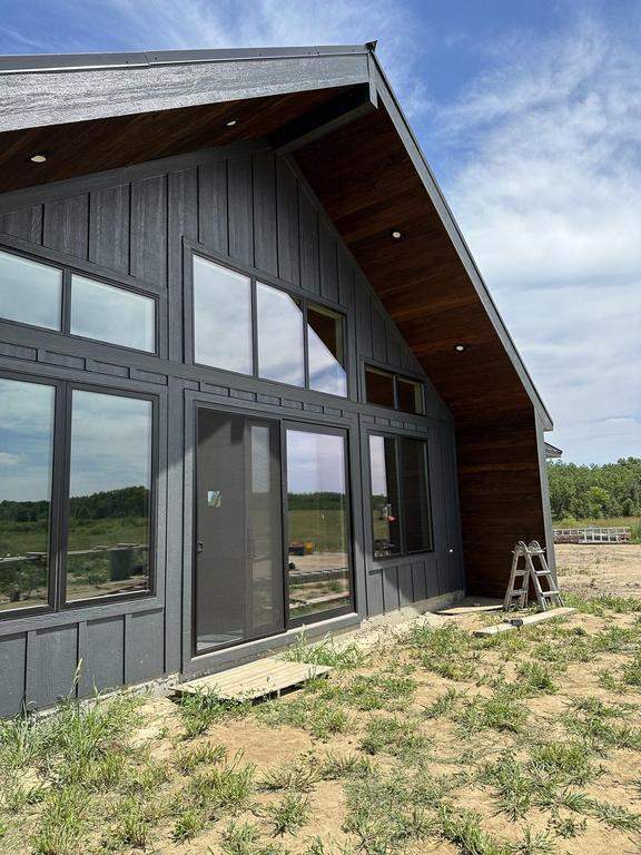 Modern home exterior with dark vertical siding, large floor-to-ceiling windows, and wood soffit installed by Precise Exteriors under a clear blue sky. Modern home exterior with dark vertical siding, large floor-to-ceiling windows, and wood soffit installed by Precise Exteriors under a clear blue sky.