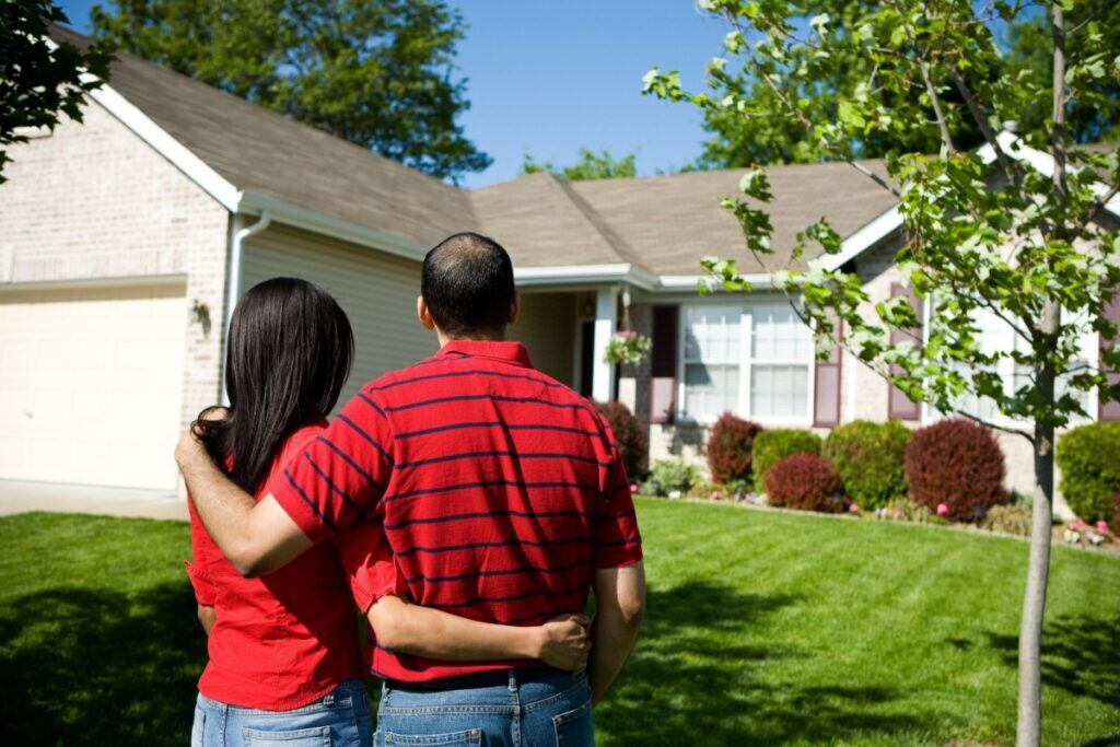 Couple standing in front of their home, admiring its exterior and roof—symbolizing homeownership and property value