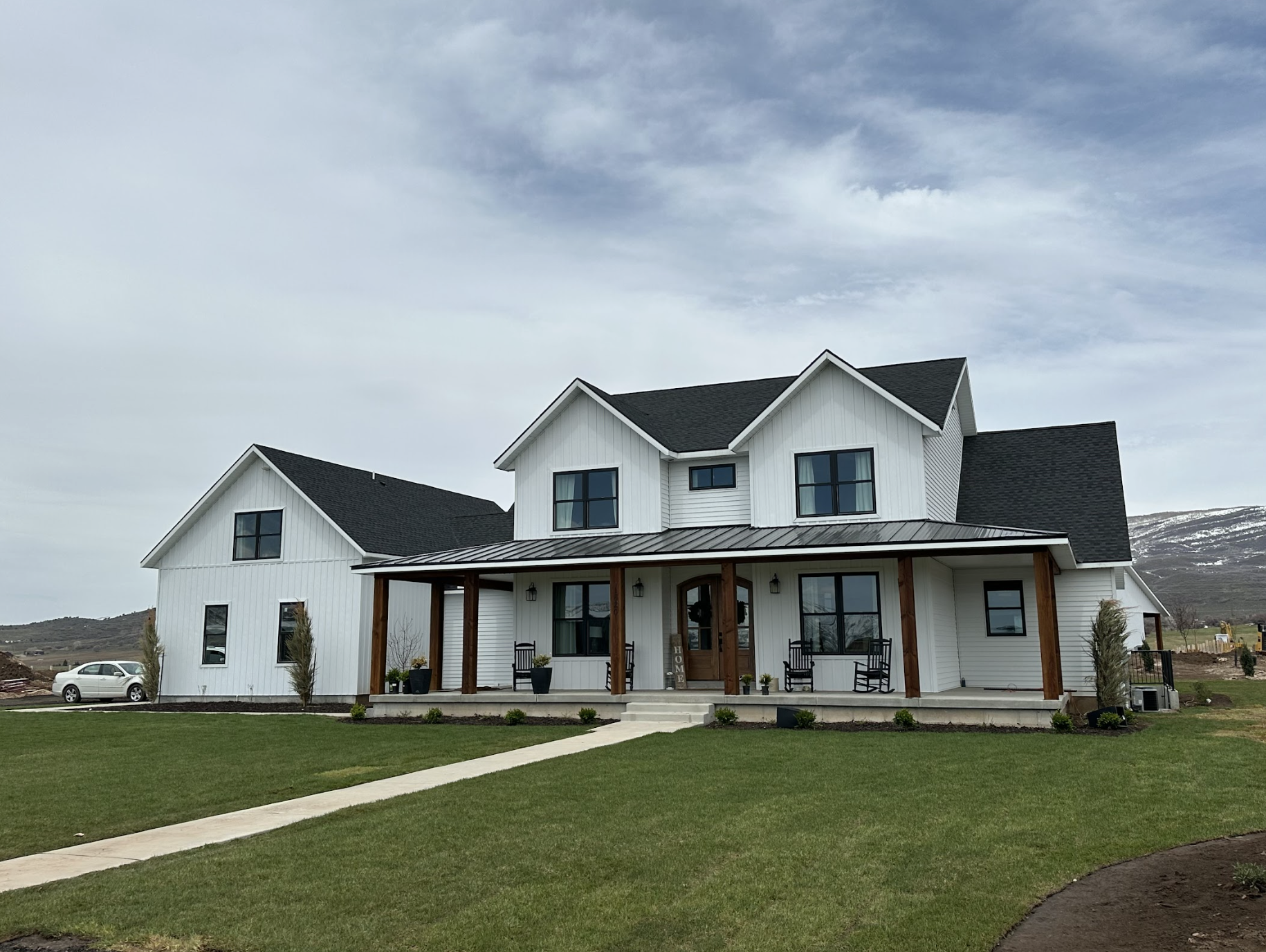 Modern white farmhouse with TruLog siding, black windows, large covered front porch with wood posts, and neatly landscaped lawn.